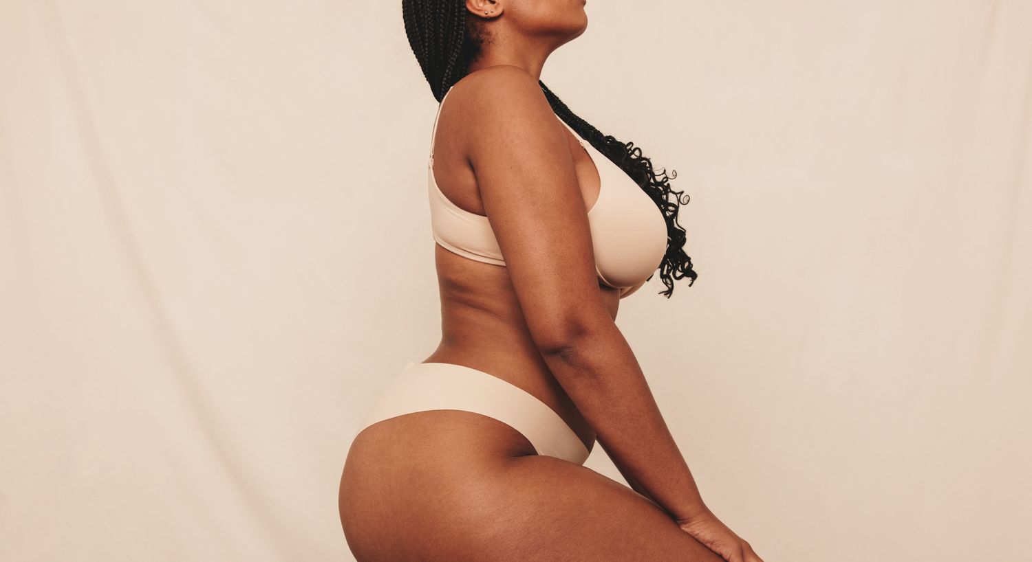 Farmington mommy makeover model posing in beige lingerie against a neutral background.