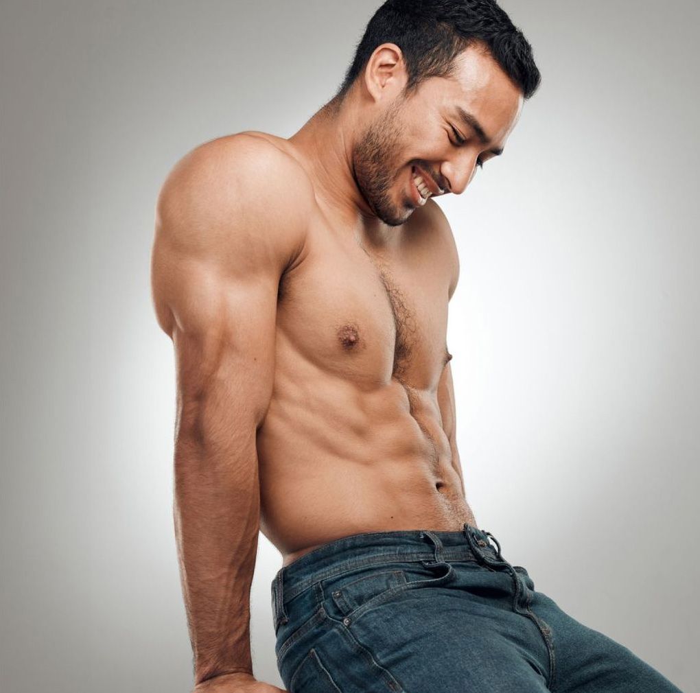 Muscular Avon gynecomastia surgery model smiling in casual denim setting.
