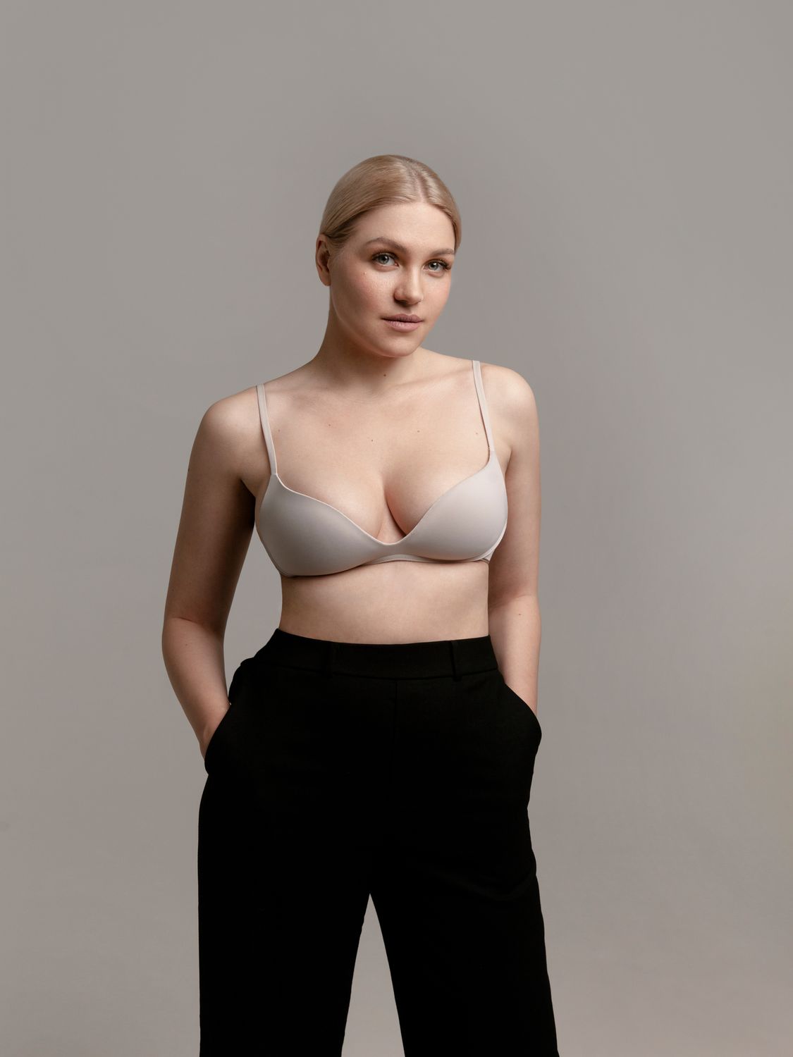 Avon breast augmentation model wearing a beige bra and black trousers.