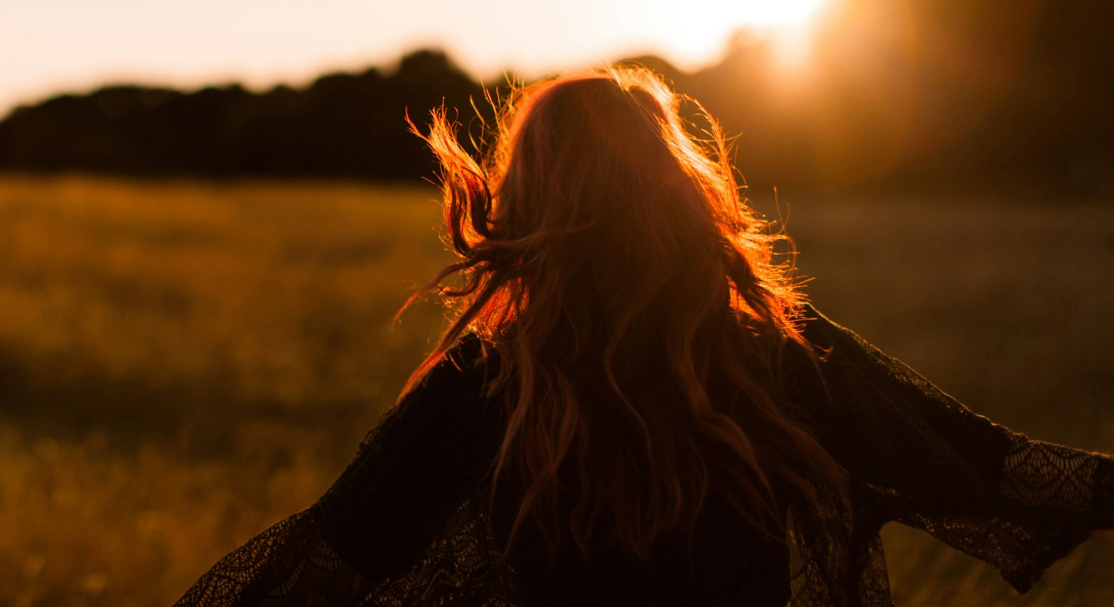 Person with flowing hair at sunset in field.